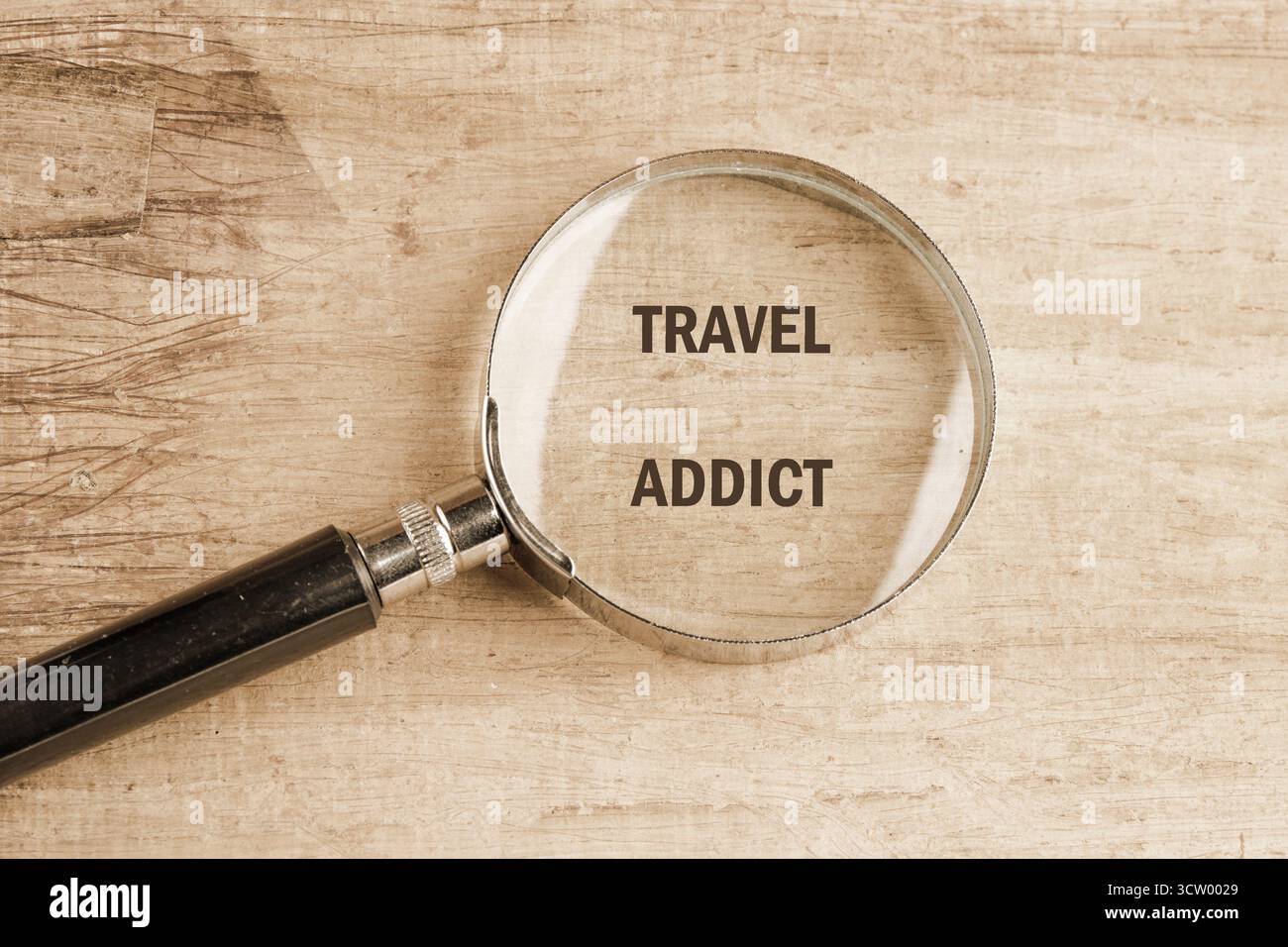 Eine Lupe fokussiert auf die Wörter REISEN SÜCHTIG auf einer strukturierten Oberfläche, die einen starken Fokus und einen intensiven Wunsch repräsentiert, die Welt zu erkunden. Stockfoto