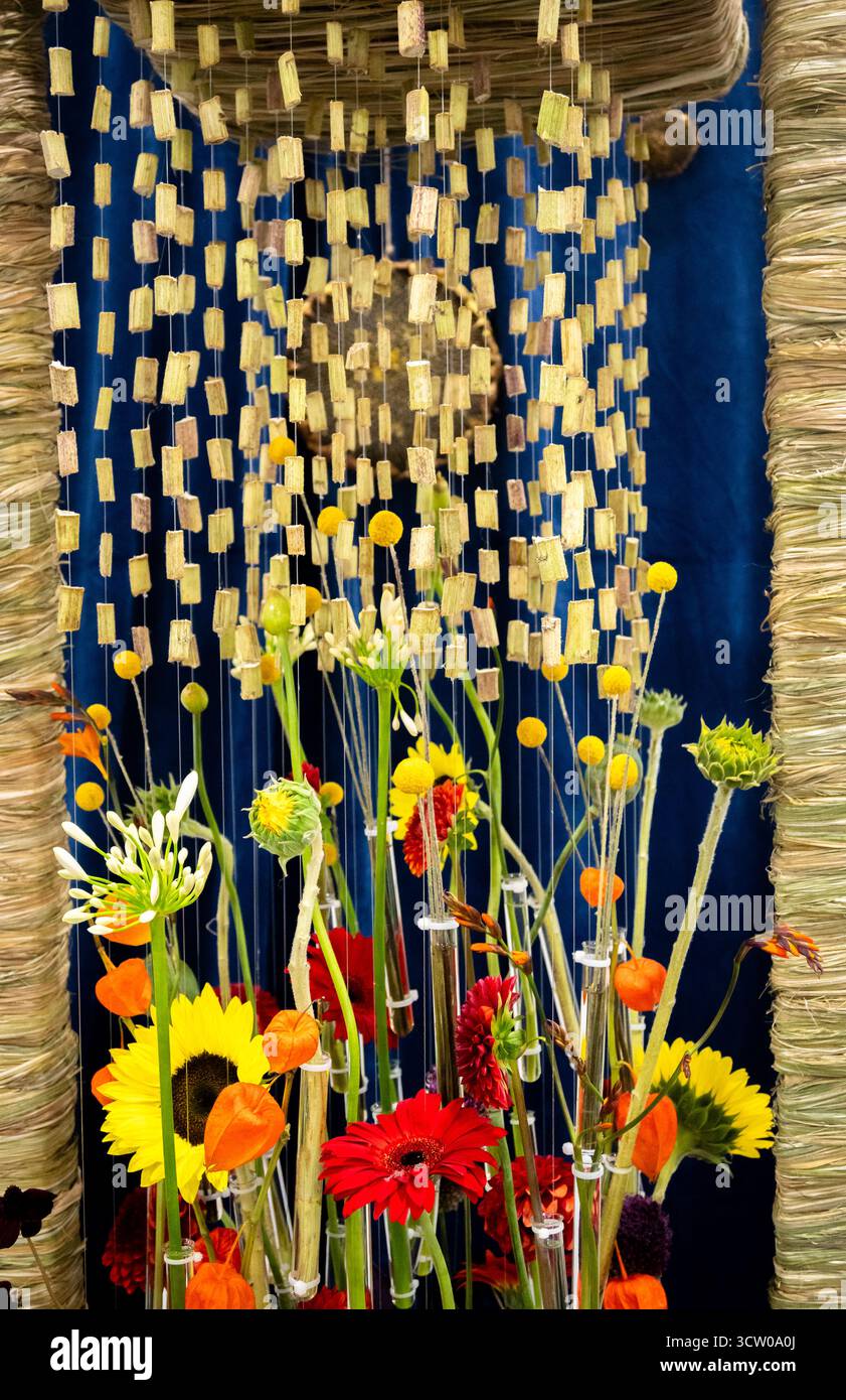 Dieses eindrucksvolle Bild zeigt eine lebendige und zeitgenössische florale Kunstinstallation mit einer eklektischen Mischung aus farbenfrohen Blüten, die einzeln aufgehängt werden Stockfoto