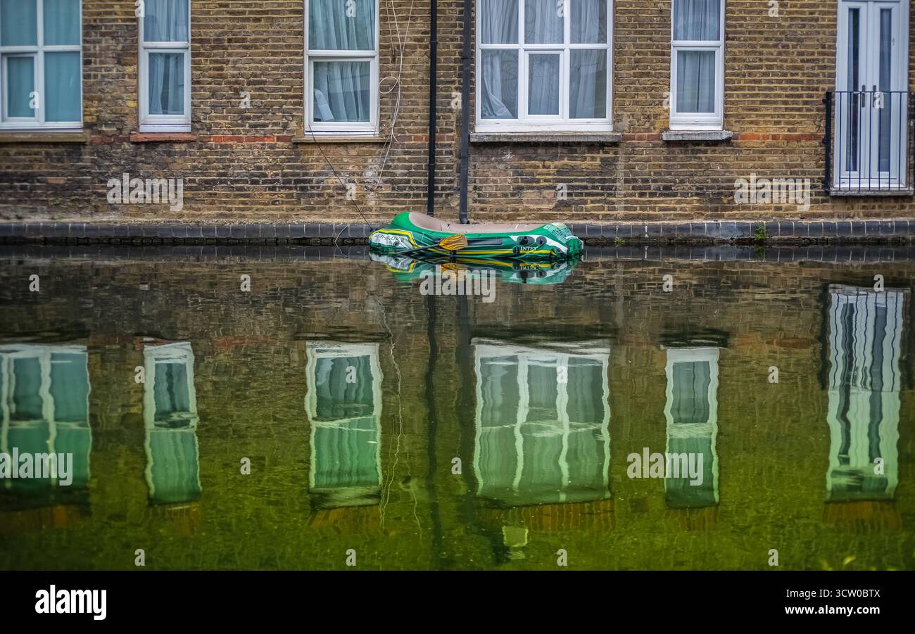 Aufblasbares Boot, das auf dem Kanalwasser schwimmt, das Backsteingebäude und Fenster reflektiert. Stockfoto