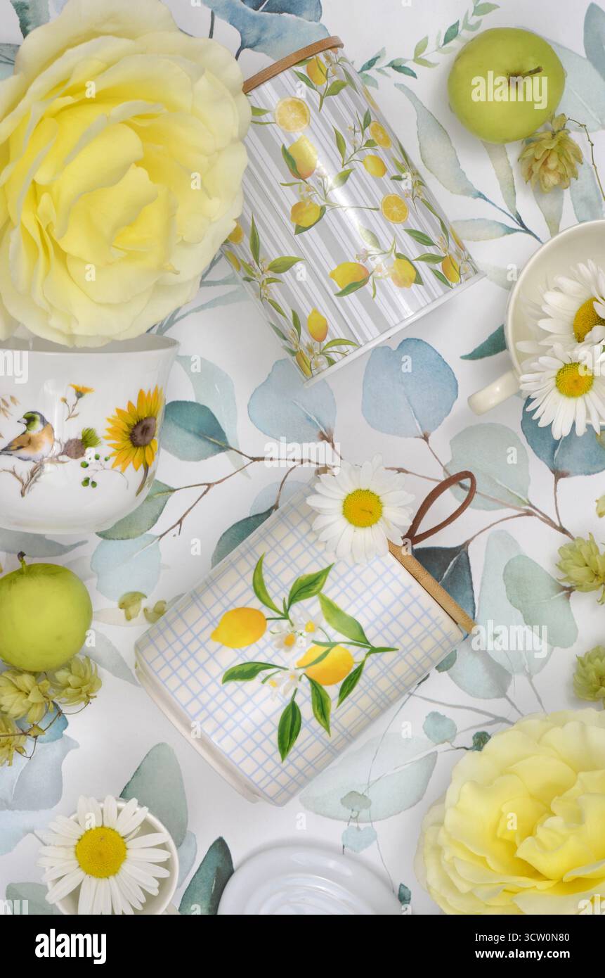 Viele gelbe Küchendekorationen: Tassen, Aufbewahrungsbehälter und Deckel. Große gelbe Rosen, grüne Äpfel und bemalte Blätter. Stockfoto