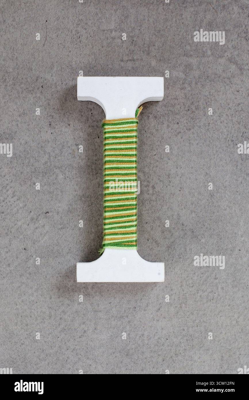 Weißer Brief, den ich aus einem Seil gemacht habe. Das Seil ist grün und gelb. Der Buchstabe befindet sich auf einer grauen Oberfläche Stockfoto