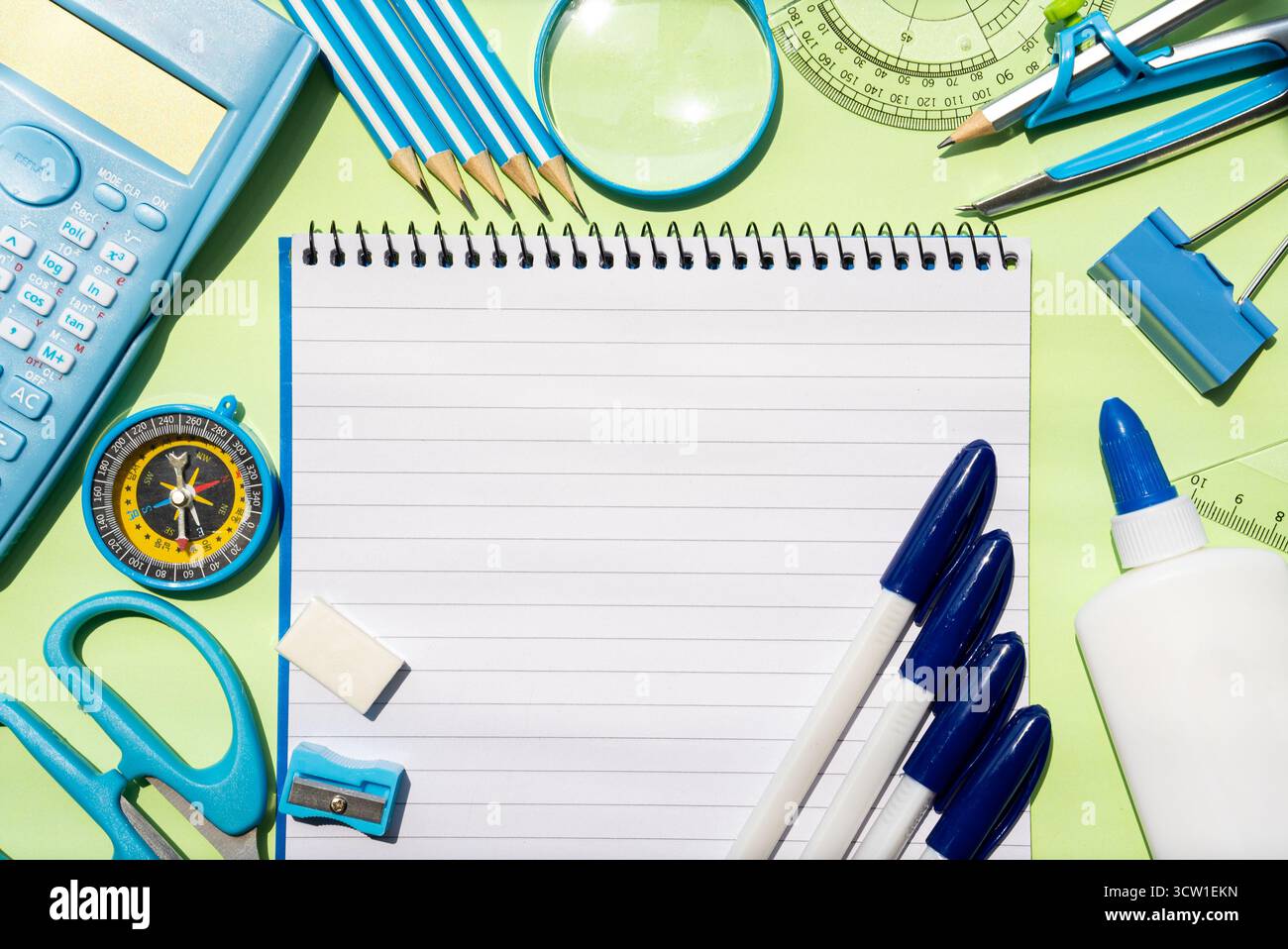 Horizontales Bild eines großen Notizbuchs, umgeben von Schere, Stiften, Kleber, Lineal, Kompass, und blauer Rechner auf grünem Hintergrund. Perfekt für Schule, Büro, kreative Projekte oder Studienplanung. Stockfoto