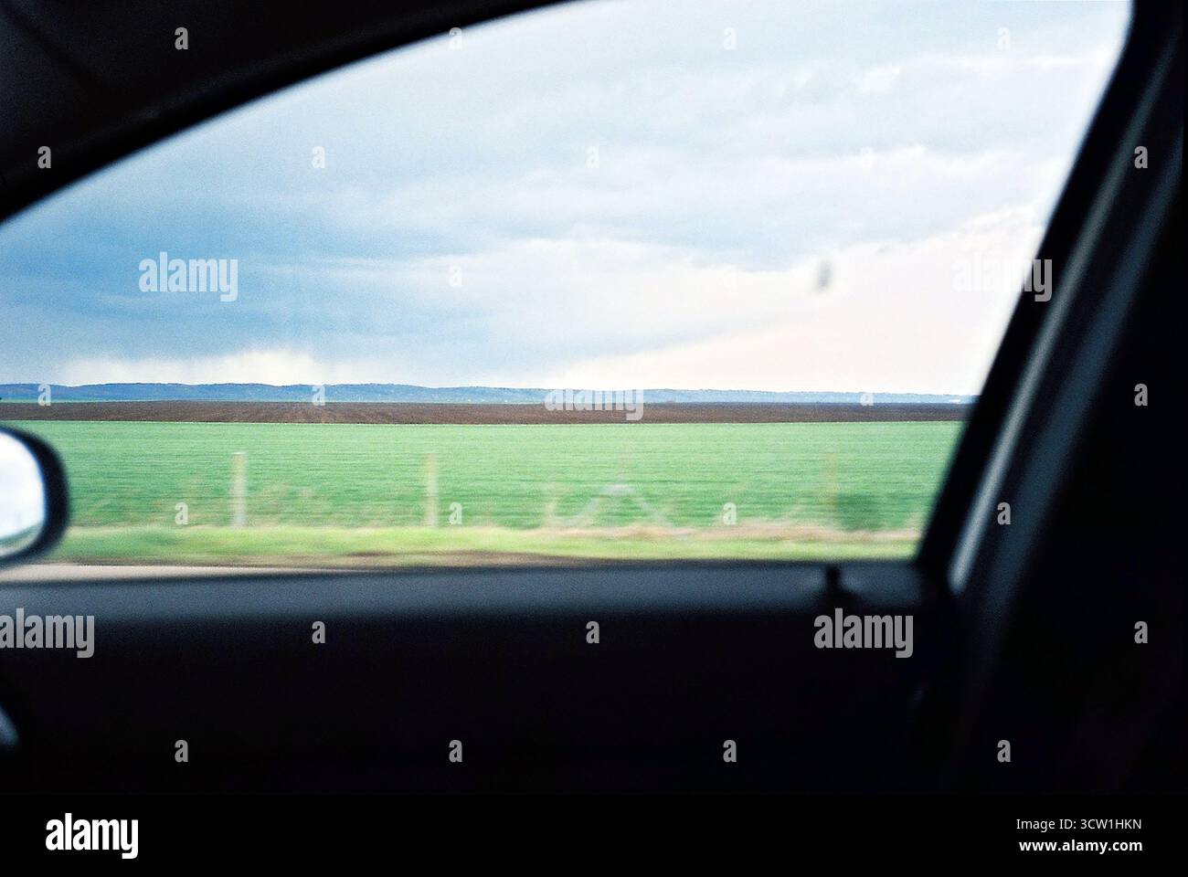 Analoges 35-mm-Foto vom Beifahrersitz mit Blick auf ein grünes Feld mit dem Berg Fruška Gora am Horizont. Ruhige und geräumige ländliche Szene. Stockfoto