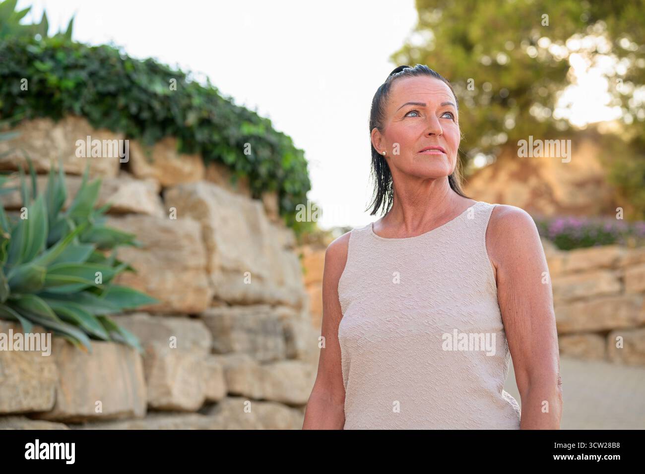 Porträt einer Reifen Frau, die vor einer Steinmauer steht und wegblickt Stockfoto