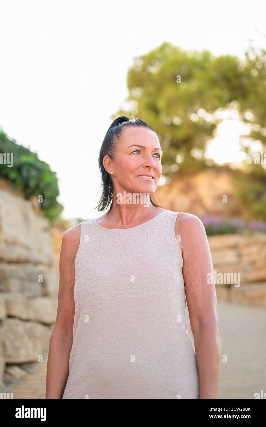 Porträt einer lächelnden skandinavischen reifen Frau, die draußen vor einer Steinmauer steht Stockfoto