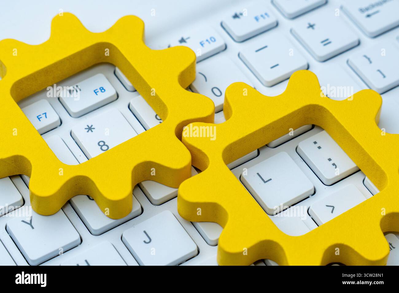 Gelbe Zahnradformen auf einer Computertastatur symbolisieren Automatisierung in Computersystemen, digitale Arbeitsabläufe und technologische Prozessintegration. Stockfoto