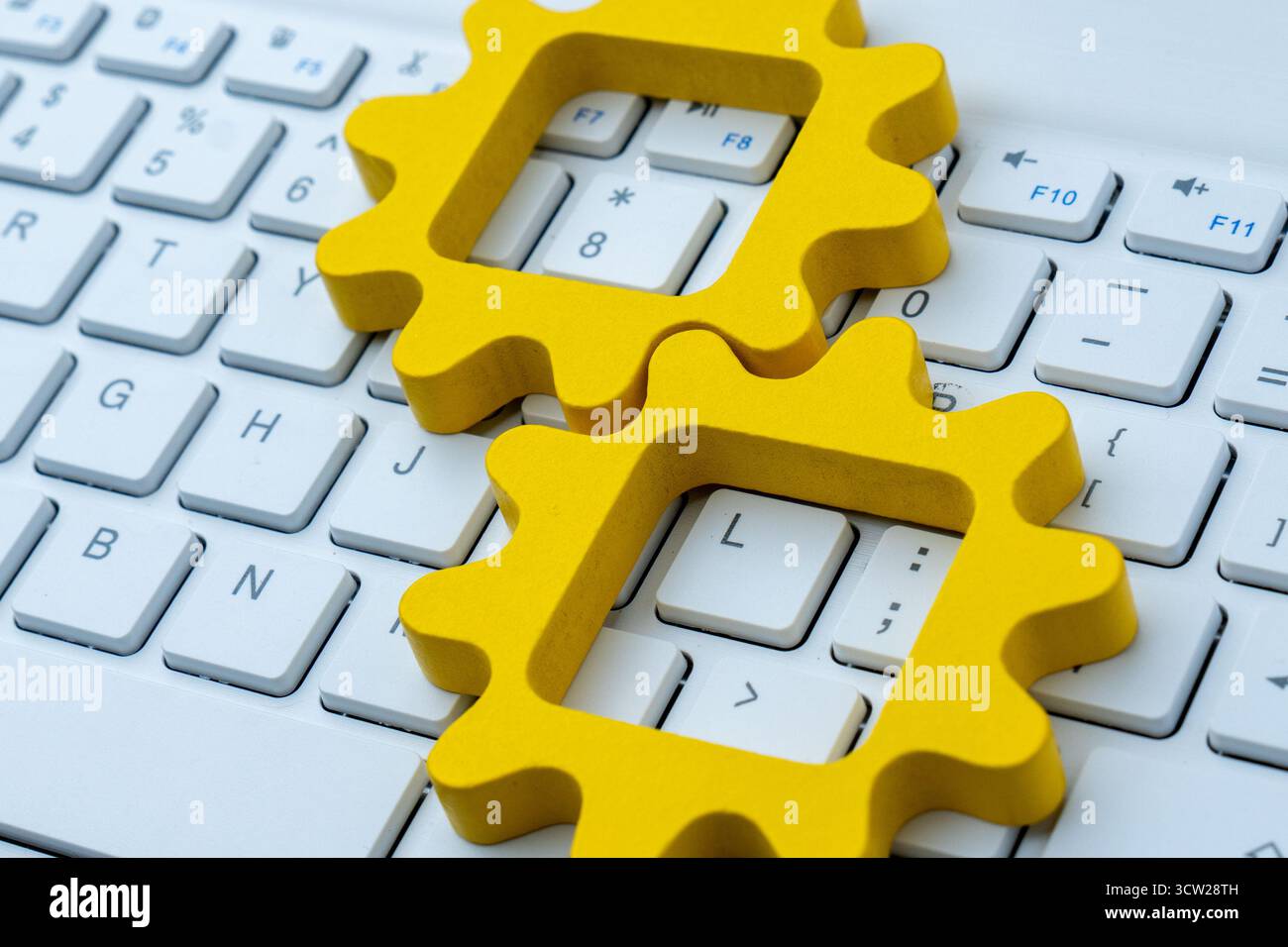 Gelbe Zahnradformen auf einer Computertastatur symbolisieren Automatisierung in Computersystemen, digitale Arbeitsabläufe und technologische Prozessintegration. Stockfoto
