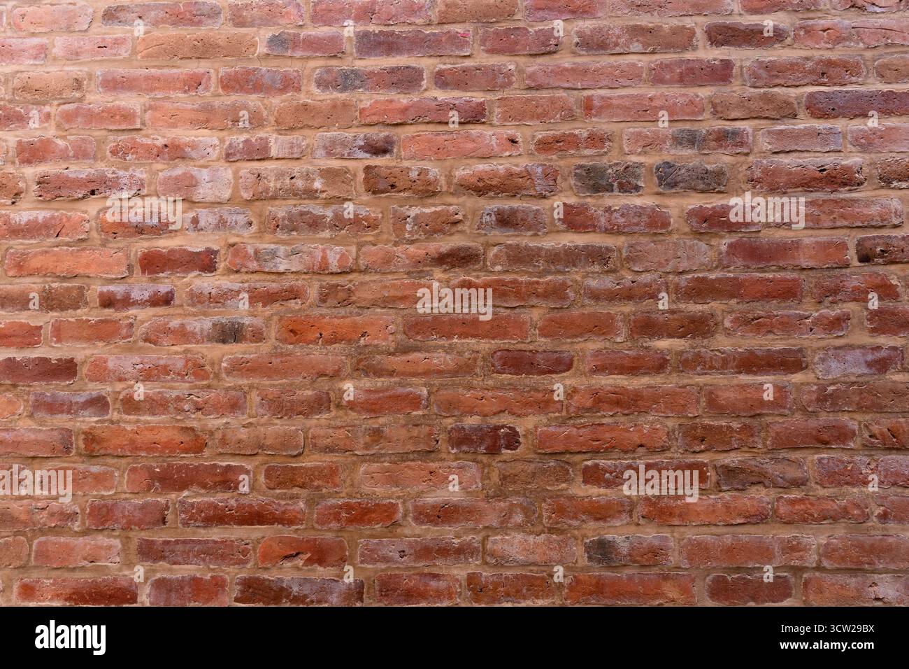 Verwitterte rote Ziegelwand mit strukturierter Oberfläche, abblätternder Farbe und natürlichen Verfärbungen, die rustikalen, alten Charakter zum Ausdruck bringen Stockfoto