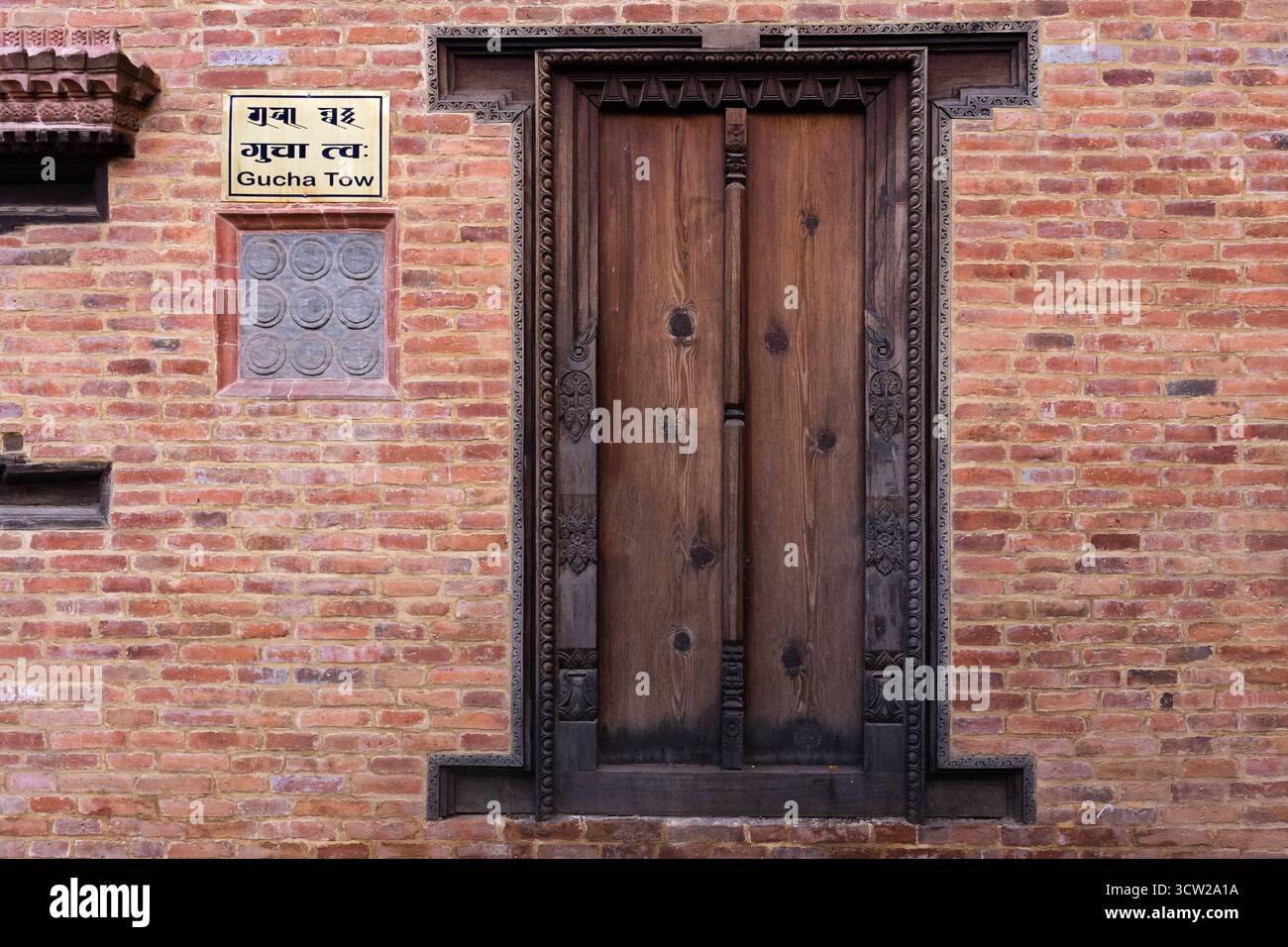 Geschnitzte Newari-Holztür in einer alten Backsteinmauer im Gucha Tow, Bhaktapur, zeigt die historische Handwerkskunst des Kathmandu-Tals Stockfoto