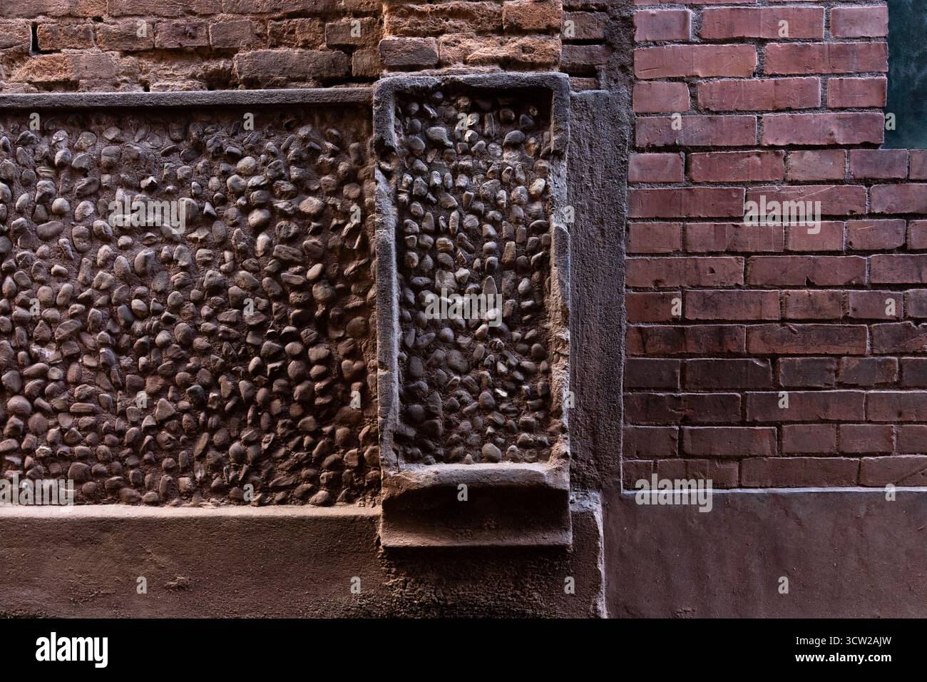 Städtische Straßenmauer mit strukturierter Kieselplatte und kontrastierenden glatten und rauen Ziegelabschnitten, die rustikale und moderne Texturen zeigen. Stockfoto