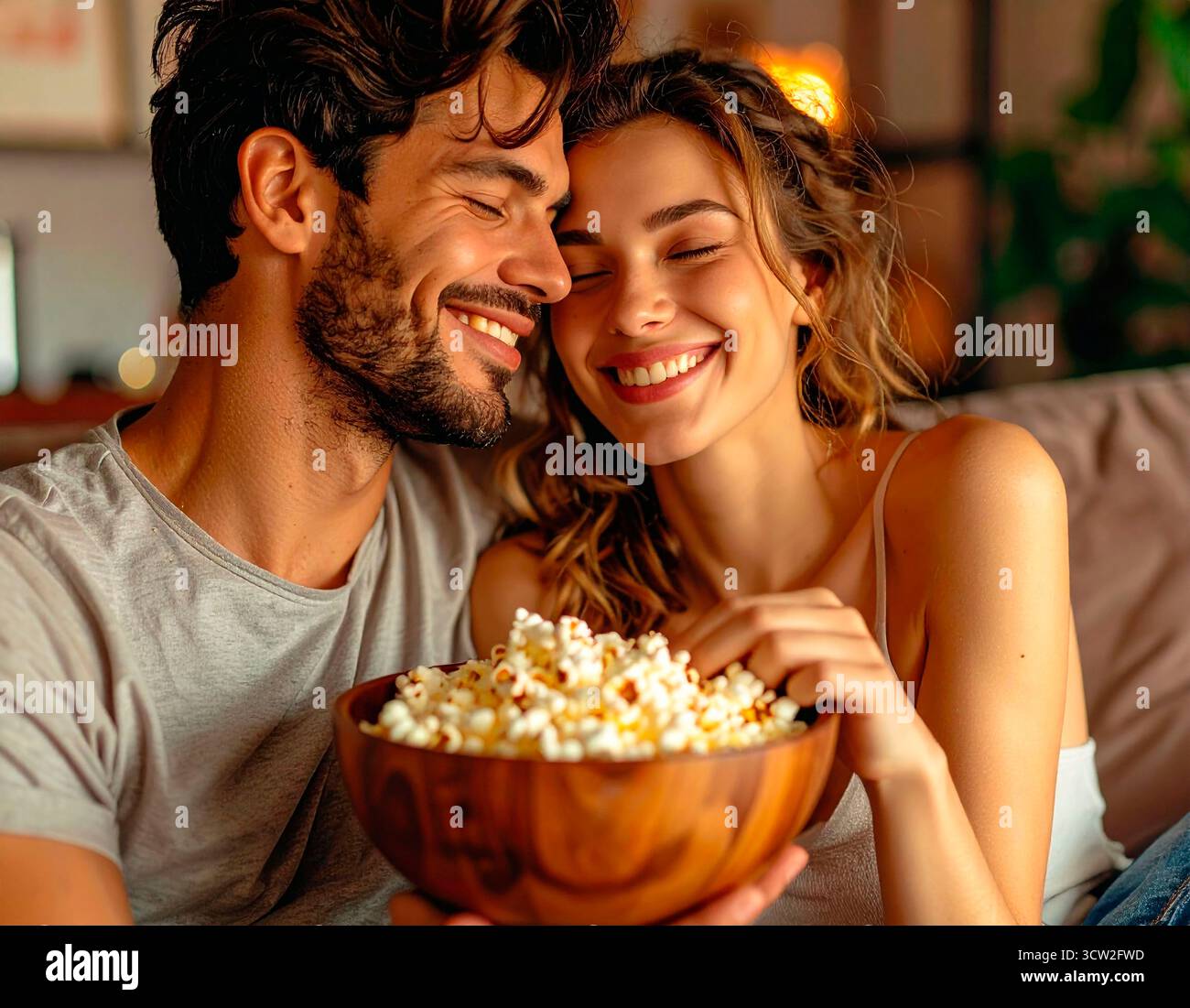 Liebende Paare, die zu Hause einen Film sehen, Popcorn teilen und lächeln Stockfoto