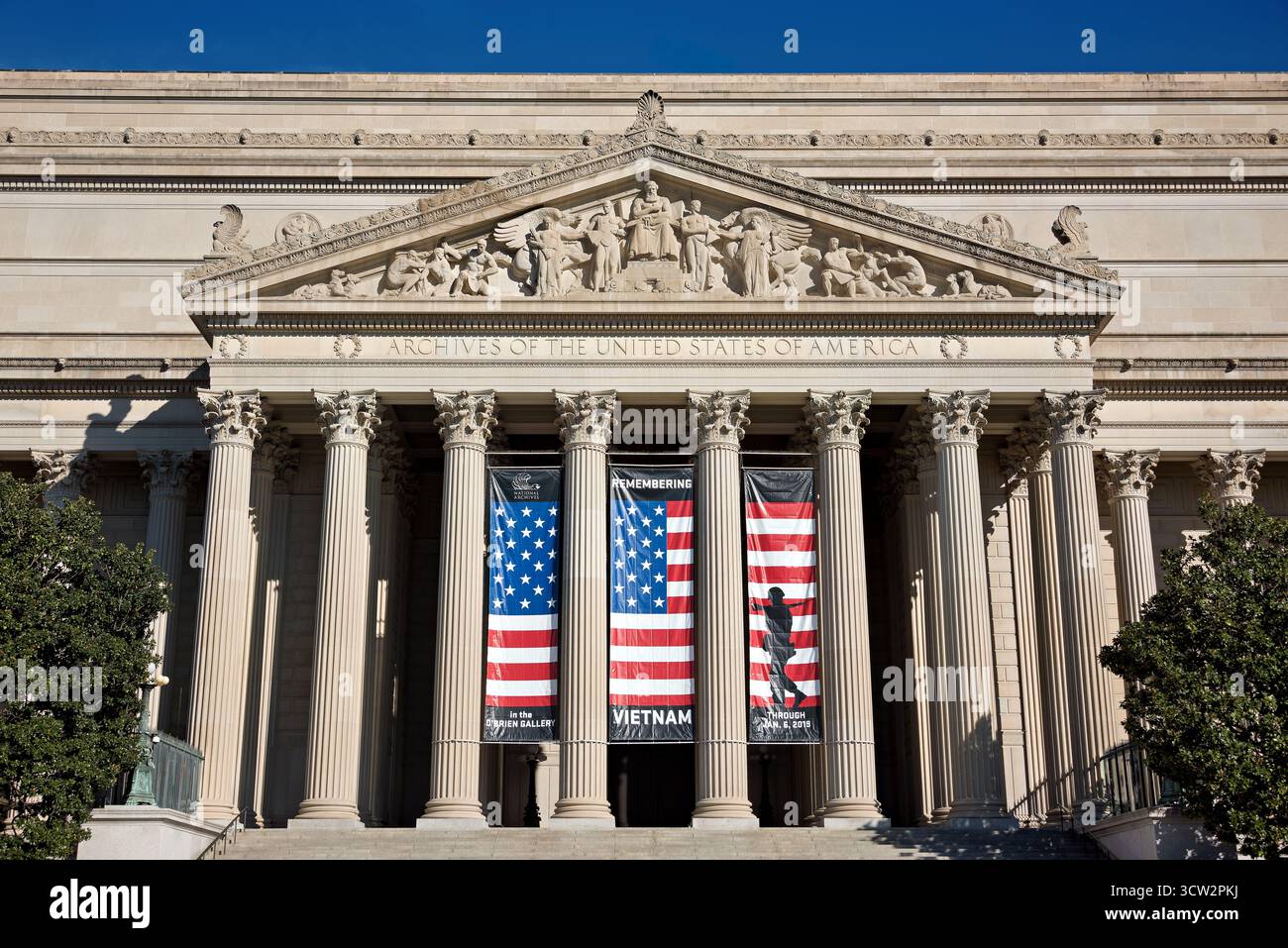Eingang der National Archives Constitution Avenue Washington DC // WASHINGTON DC – das Gebäude des National Archives an der Constitution Avenue verfügt über eine große neoklassizistische Fassade mit einem markanten Portikus und korinthischen Säulen. Der Giebel über dem Eingang zeigt Adolph A. Weinmans Skulptur, den Recorder of the Archives und die Inschrift „ARCHIVE OF THE UNITED STATES OF AMERICA“. Zwischen den Säulen sind Banner für die Ausstellung „Remember Vietnam“ zu sehen, die bis zum 6. Januar 2019 lief. Diese Institution bewahrt wesentliche historische Aufzeichnungen der Vereinigten Staaten, einschließlich des Dekl Stockfoto