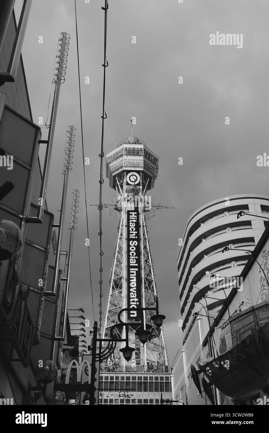 Monochromer Blick auf den Tsutenkaku-Turm, der sich zwischen Gebäuden im Shinsekai-Viertel von Osaka erhebt. Stockfoto