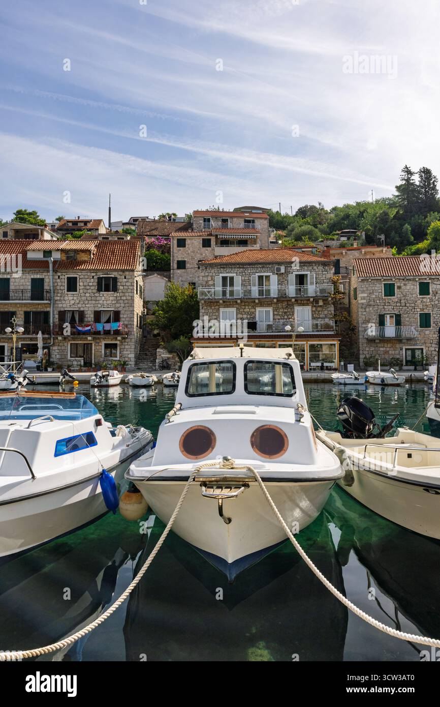 Eine ruhige Hafenszene in einem kleinen Steindorf, farbenfrohe Boote, die an den Kai gebunden sind, rustikale Häuser mit roten Dächern, ruhiges Wasser und klarem blauem Himmel Stockfoto
