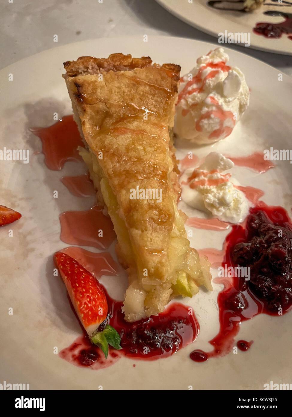 Apfelstrudelscheibe mit Vanilleeis, Erdbeermarmelade und frischer Erdbeere auf einem Teller in Restaurant-Atmosphäre - Smartphone-aufgenommenes Stockfoto