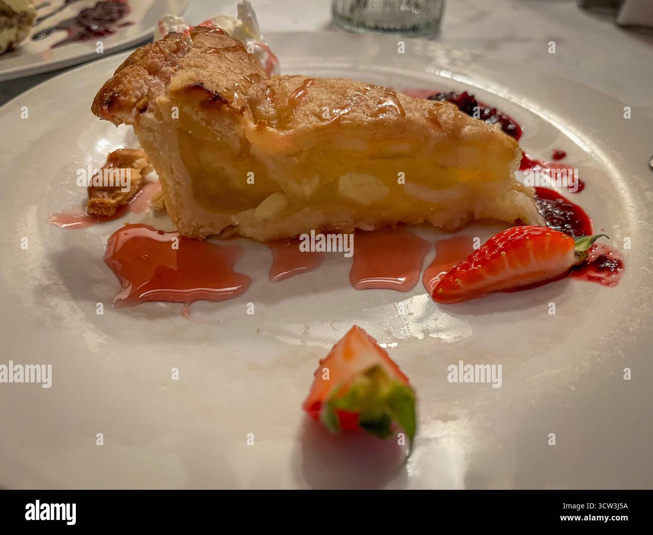 Apfelstrudelscheibe mit Vanilleeis, Erdbeermarmelade und frischer Erdbeere auf einem Teller in Restaurant-Atmosphäre - Smartphone-aufgenommenes Stockfoto