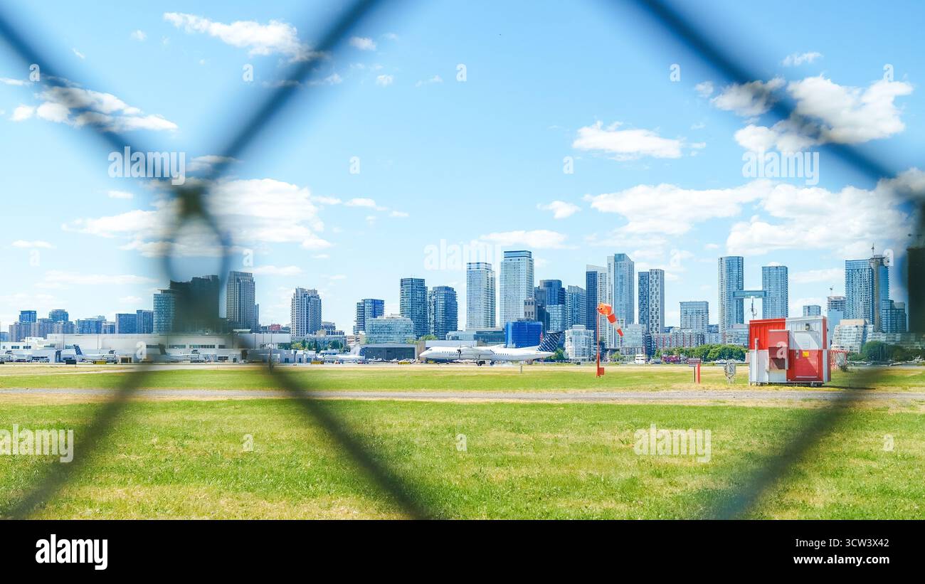 Toronto ON, Kanada - 4. Juli 2022: Blick auf die Skyline der Stadt durch einen Maschendrahtzaun, mit Wolkenkratzern und leuchtendem grünem Gras im Vordergrund Stockfoto