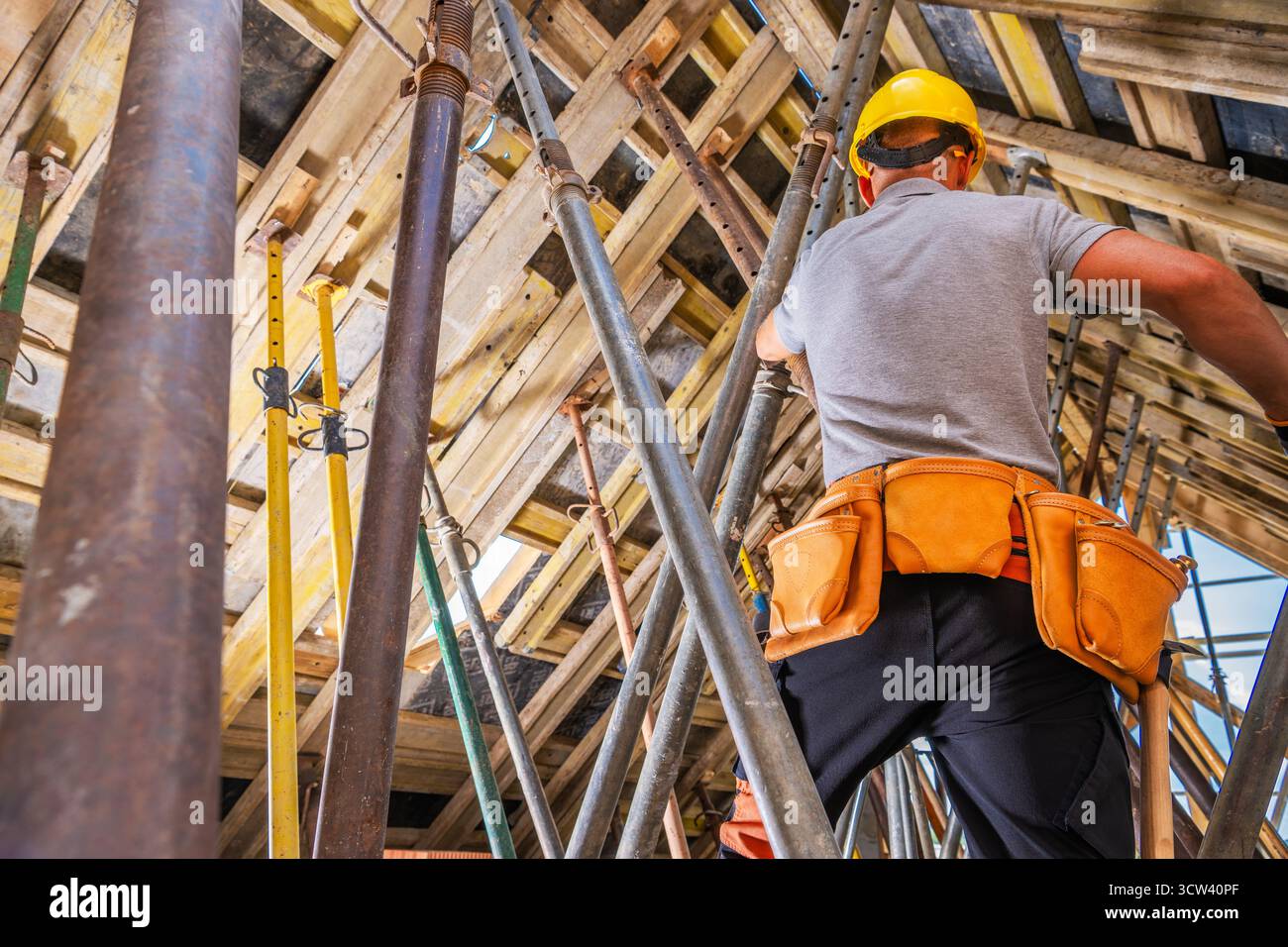 Ein Bauarbeiter mit Helm und Gurtzeug montiert Gerüste auf einem Hochhaus, wobei er sich tagsüber auf Sicherheit und Präzision konzentriert. Stockfoto