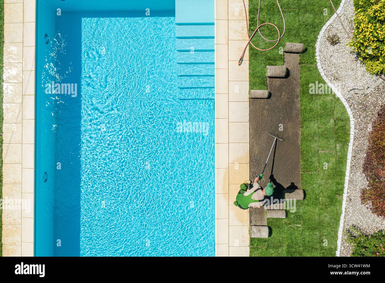 Eine Person reinigt den Pool, während die Sonne scheint, umgeben von einem gepflegten Rasen und Garten. Die ruhige Szene ist ein Höhepunkt der Sommerferien. Stockfoto