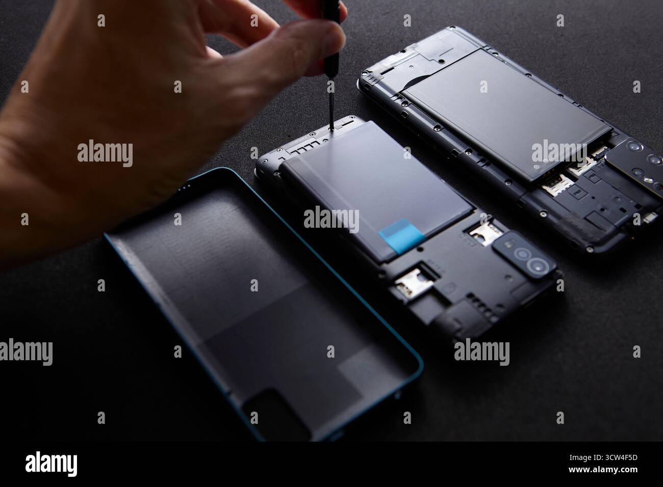 Techniker Hand mit Schraubendreher, der auf schwarzer Oberfläche an Smartphone-Teilen arbeitet. Die Detailansicht symbolisiert Technologie-Service, Elektronik-Reparatur und Stockfoto