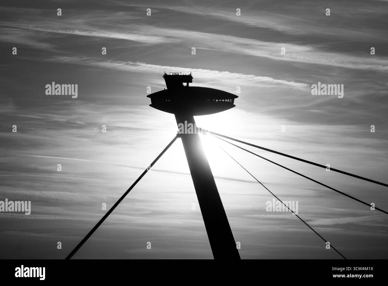 Ein hoher Turm steht mit der Silhouette, während die Sonne hinter ihm untergeht, und wirft einen dramatischen Schatten über die Landschaft mit weichen Wolken am Himmel. Stockfoto