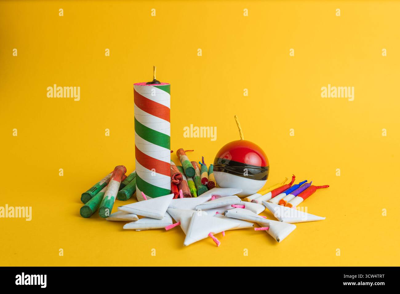 Komposition einer Vielzahl von festlichen Pyrotechniken, einschließlich Raketen, einer Kugel und dreieckigen Feuerwerkskörpern, auf einem leuchtend gelben Hintergrund. Stockfoto