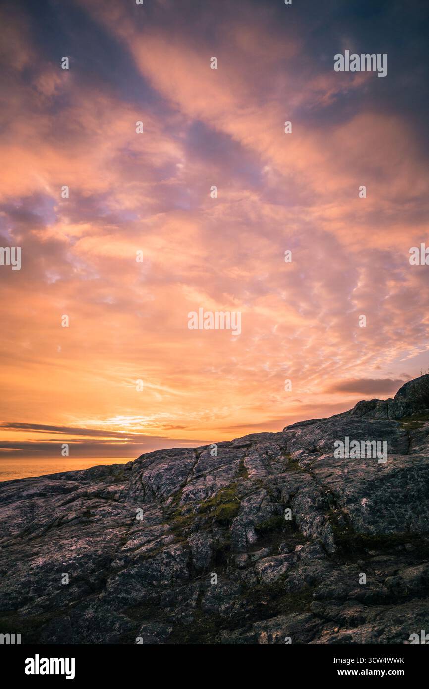 Leuchtende Farben erfüllen den Himmel während des Sonnenuntergangs und strahlen ein warmes Leuchten über einer felsigen Küste aus. Die Szene fängt die Schönheit der Natur und die beruhigende Atmosphäre ein Stockfoto
