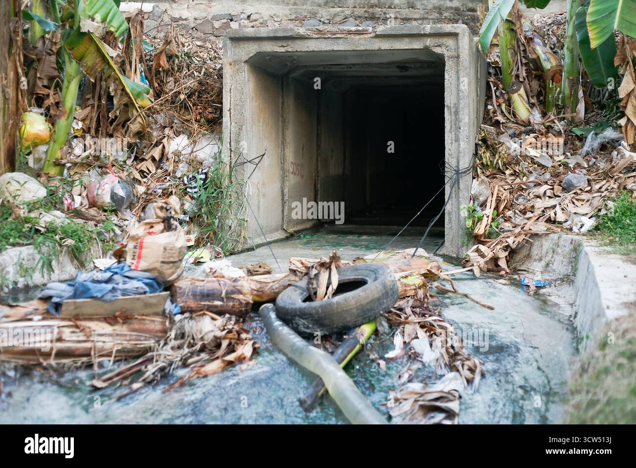 Verschmutzter Austritt des Abflusskanals mit Müll und Autoreifen Stockfoto
