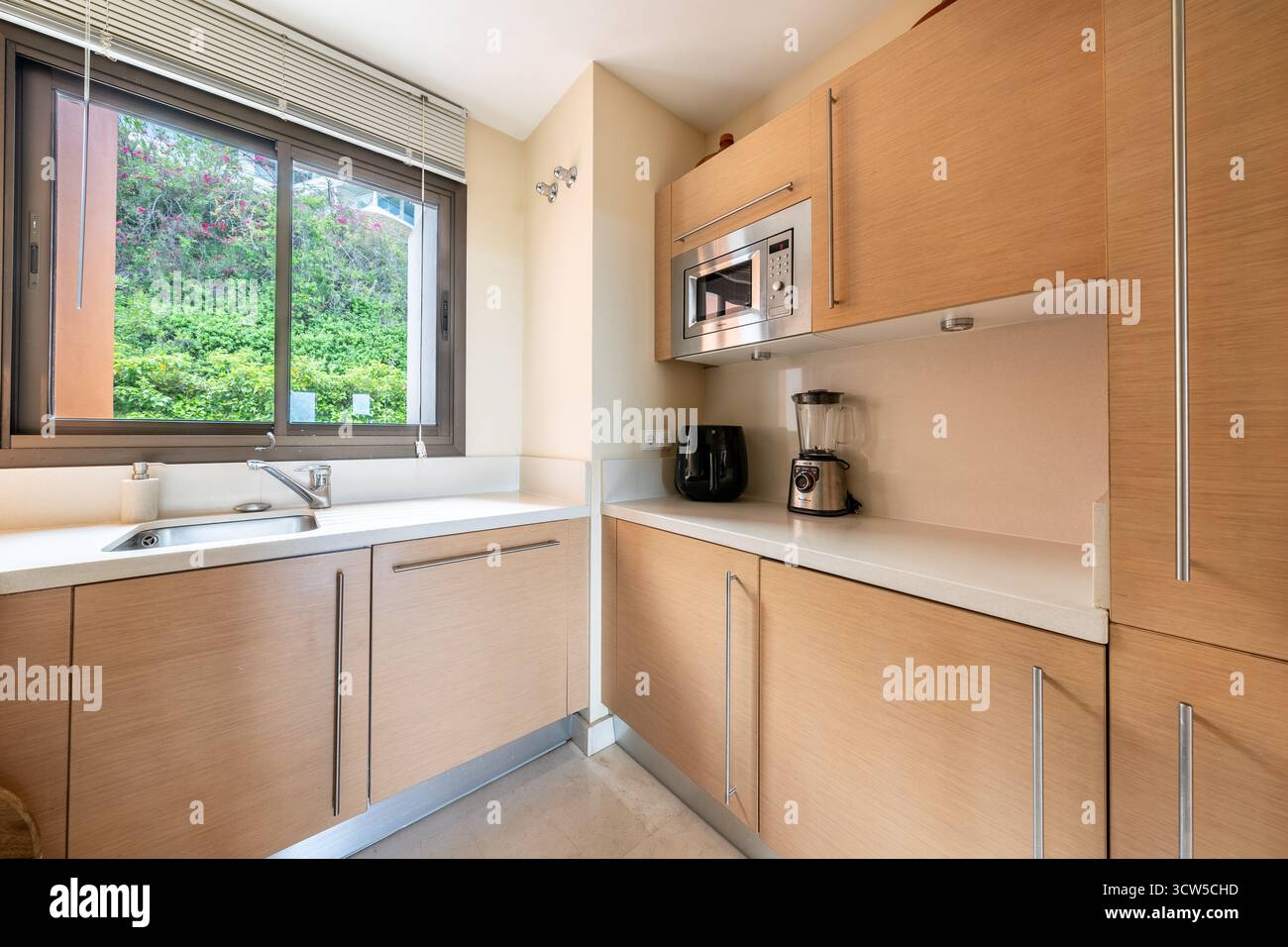 Moderne Kochnische mit hellen Holzschränken und weißen Arbeitsplatten in mediterraner Immobilie Stockfoto