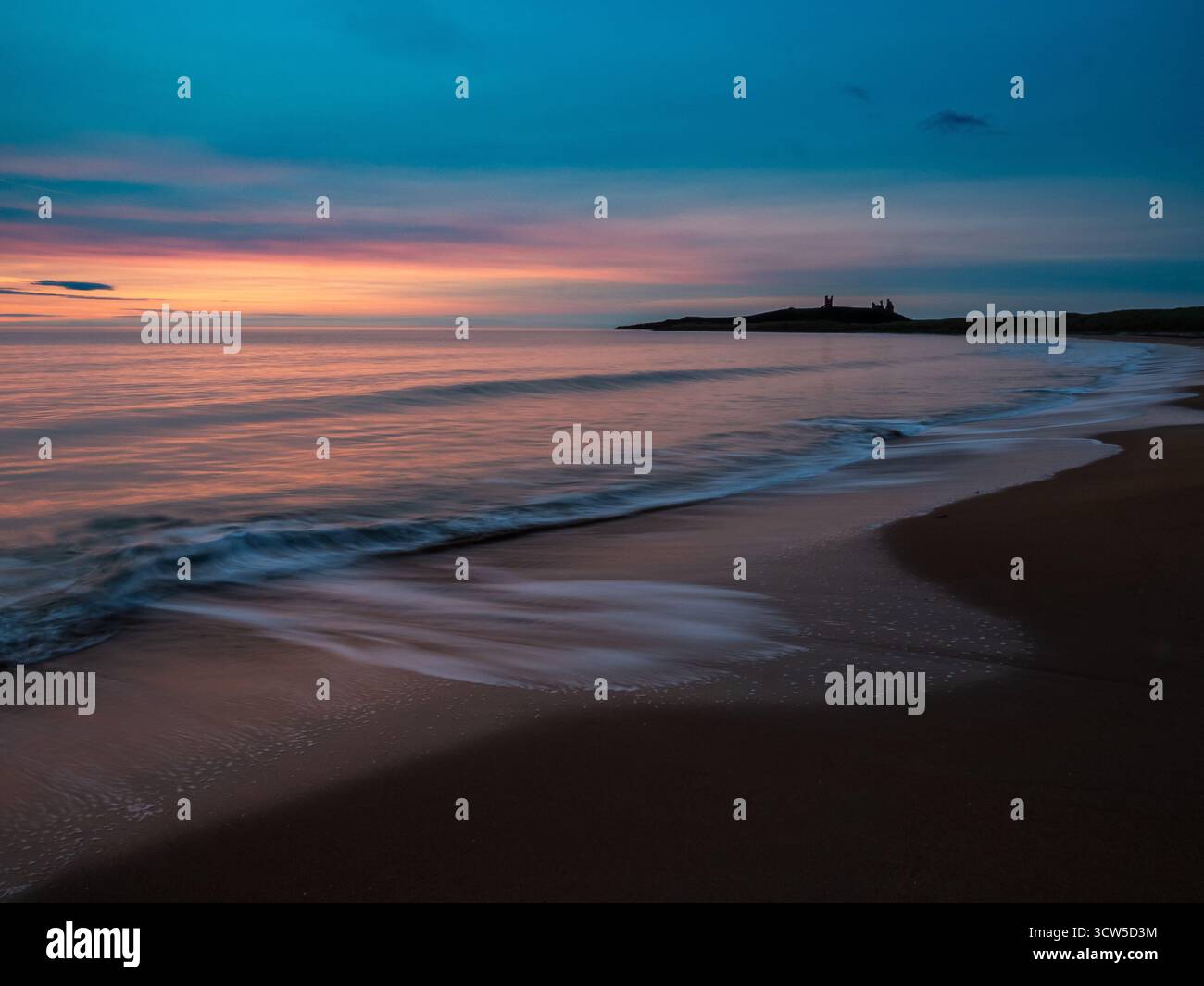 Dunstanburgh Castle bei Sonnenaufgang mit Blick über das ruhige Meer und den Sandstrand bei Sonnenaufgang Stockfoto