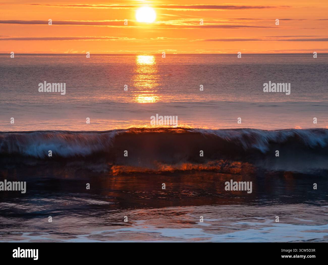 Brechende Welle, die im Sonnenaufgangslicht leuchtet und über das ruhige Meer reflektiert Stockfoto