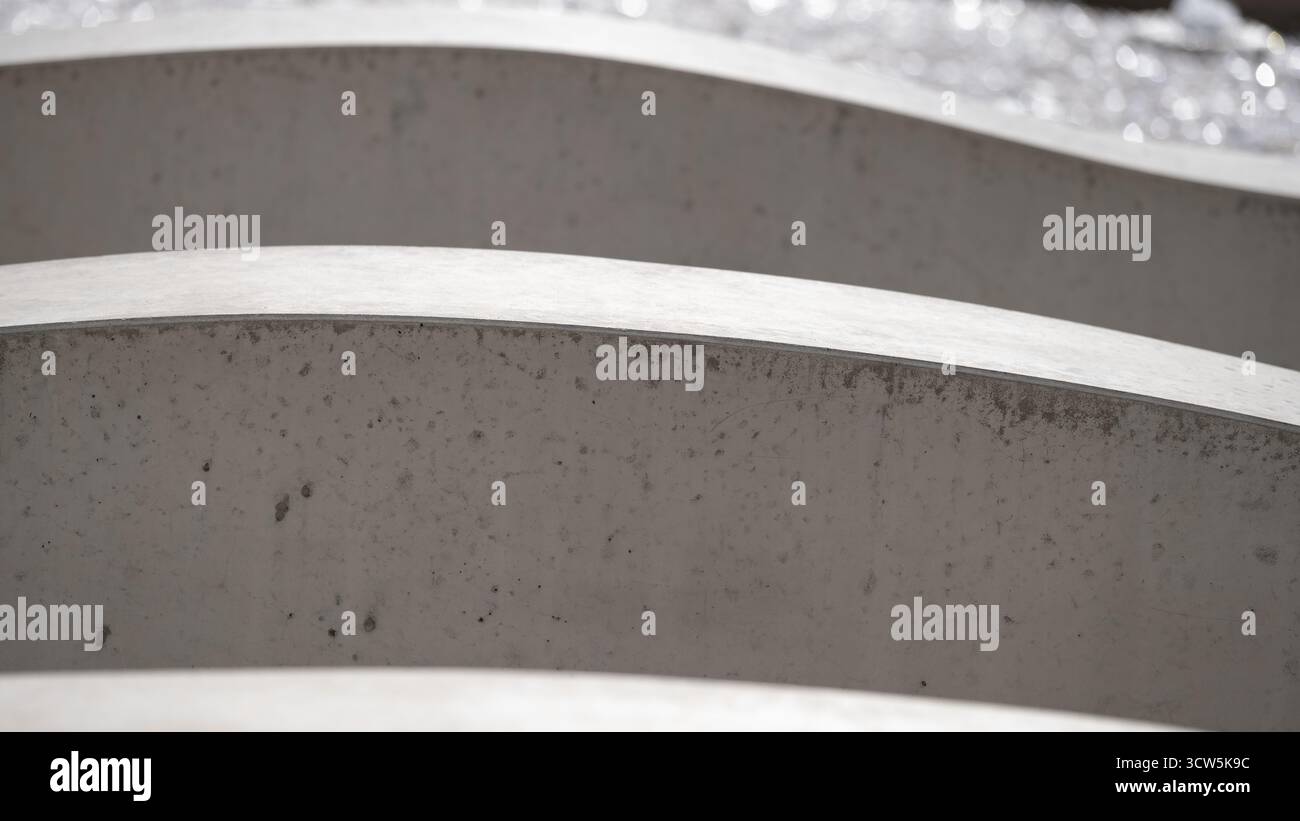 Nahaufnahme gekrümmter Betonelemente, die ein abstraktes architektonisches Muster bilden. Minimalistisches, modernes Design mit sich wiederholenden Linien und weichen Schatten. Concep Stockfoto