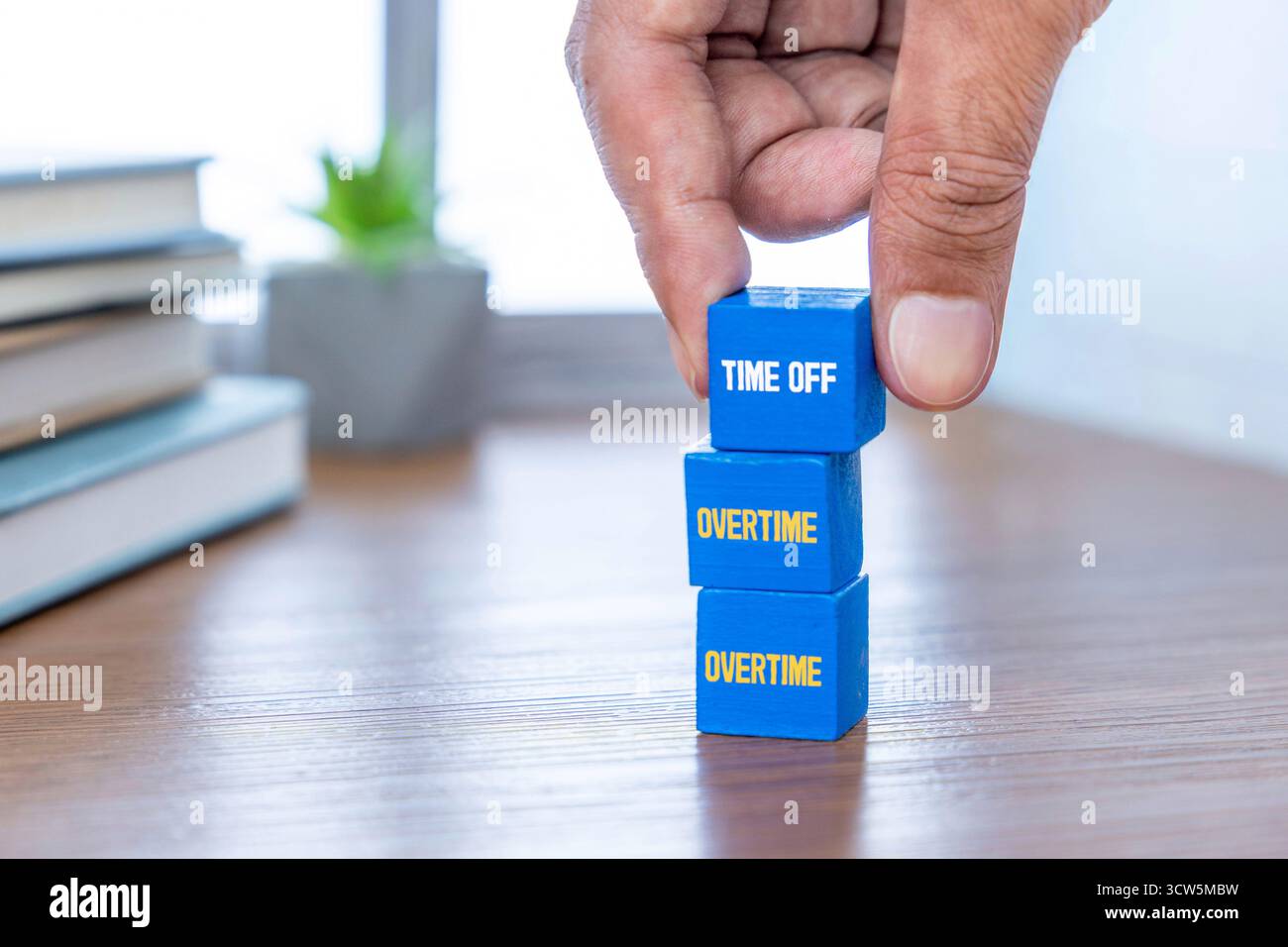 Eine Hand stapelt blaue Holzblöcke mit der Aufschrift ÜBERSTUNDEN und FREIZEIT auf einen Schreibtisch. Work-Life-Balance, Zeitmanagement, Vergütung, Ruhekonzept. Stockfoto