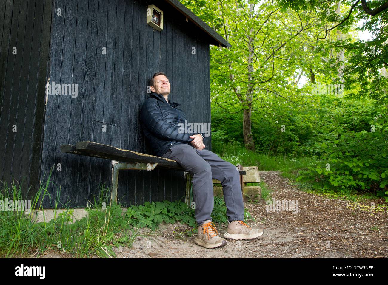 Mann im friedlichen Moment auf Bank im Wald genießt die Natur, Mann lehnt sich an Holzschuppen und glücklich im Naturmoment Stockfoto