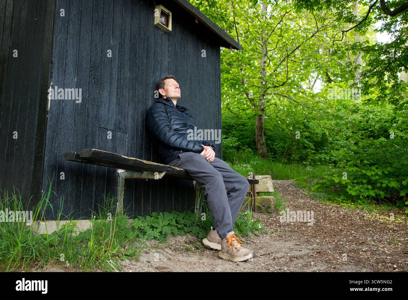 Mann im friedlichen Moment auf Bank im Wald genießt die Natur, Mann lehnt sich an Holzschuppen und glücklich im Naturmoment Stockfoto