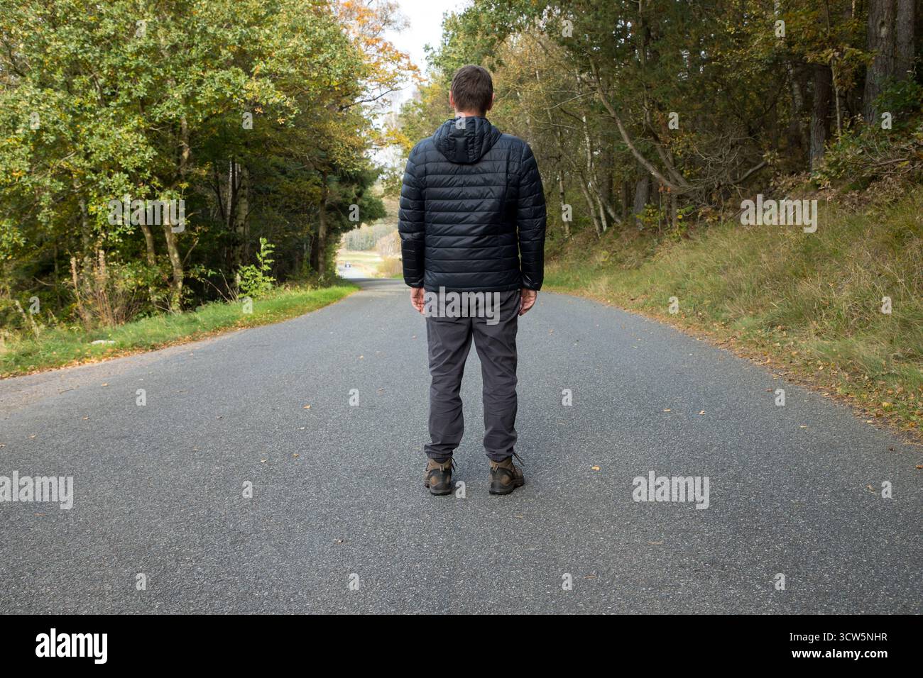 Mann, der auf Asphaltstraße steht, Rückblick, der nach vorne blickt und denkt, was im Leben vor uns liegt, welche Entscheidungen zu treffen sind, wo mein Leben hin geht, Entscheidungen Stockfoto