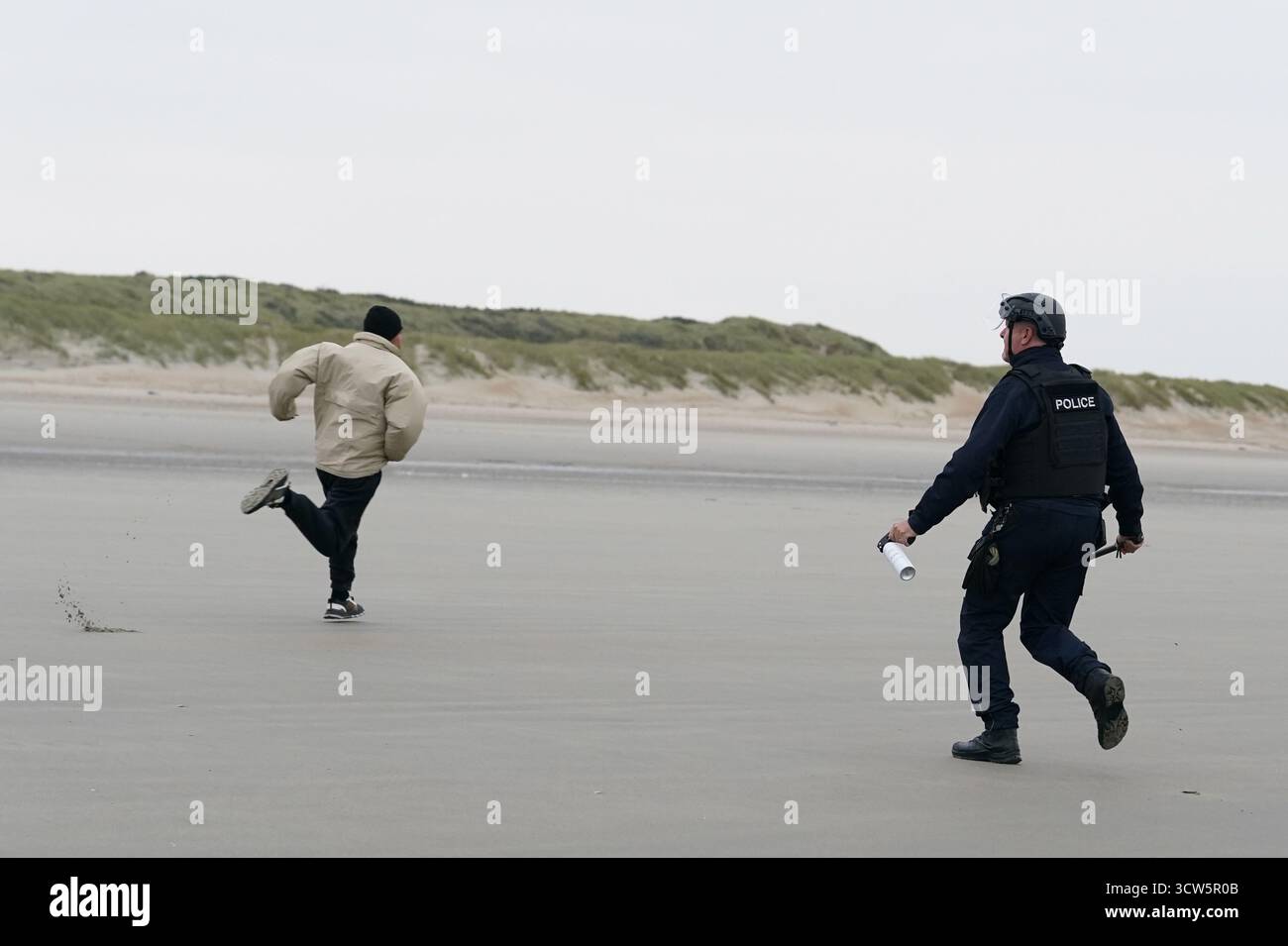 Ein französischer Polizist jagt Menschen, die als Migranten gelten, am Strand in Gravelines, Frankreich, und besprüht sie mit einer Substanz. Bilddatum: Freitag, 10. Oktober 2025. Stockfoto