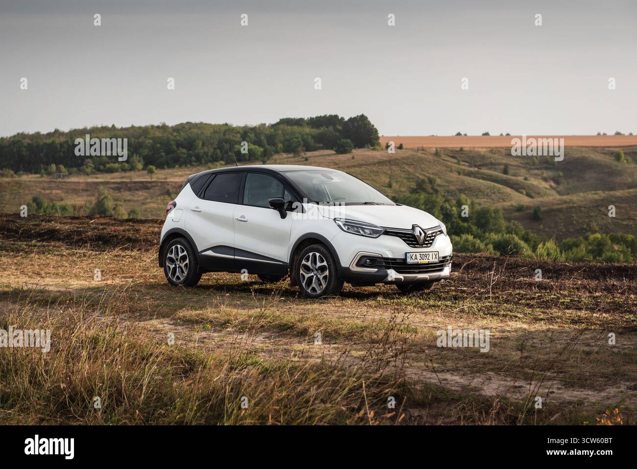 Weißer Renault Captur auf trockener Wiese. Vordere Dreiviertelansicht des kompakten Crossover-SUV in hügeliger ländlicher Umgebung. Stockfoto