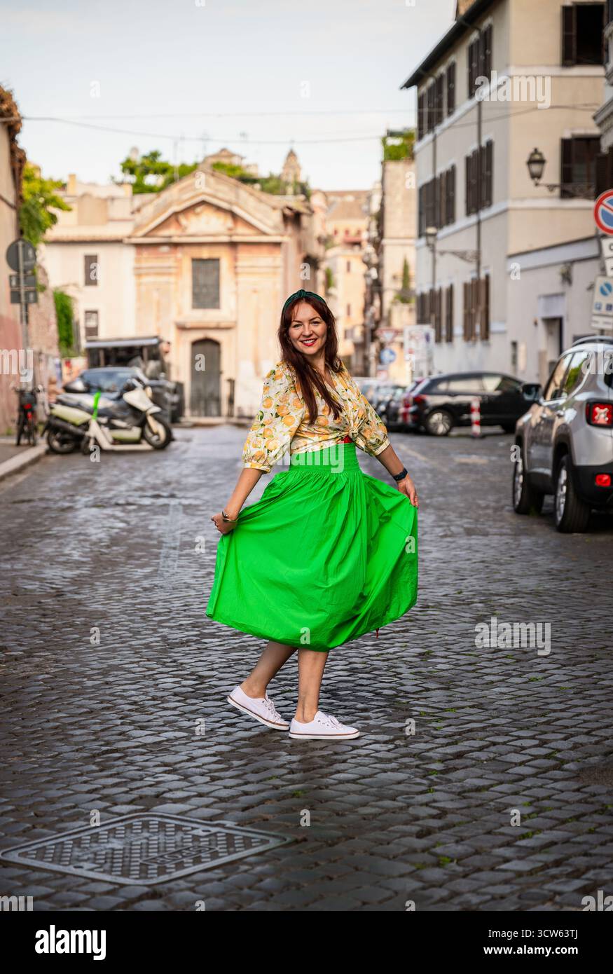 Frau im grünen Rock, die auf der Kopfsteinpflasterstraße in Rom, Italien, läuft Stockfoto
