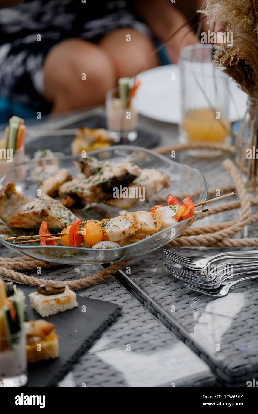 Nahaufnahme eines klaren Gerichts mit gebackenen Fischstücken und Gemüsespießen mit Kräutern. Gemischte gebratene Fisch- und Hühnerkebabs mit rotem Pfeffer und Kräutern Stockfoto