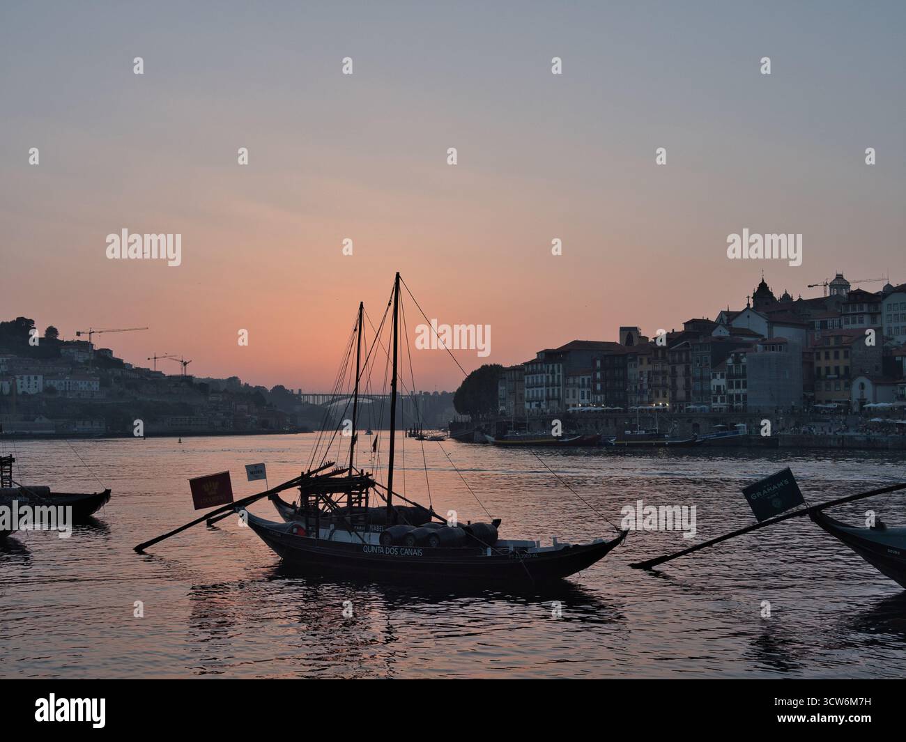 Rabelo-Boote auf dem Fluss Douro in der Abenddämmerung in Porto, Portugal - Silhouetten von Rabelo-Booten mit Fässern auf dem Fluss Douro bei Sonnenuntergang, mit historischen Sehenswürdigkeiten Stockfoto