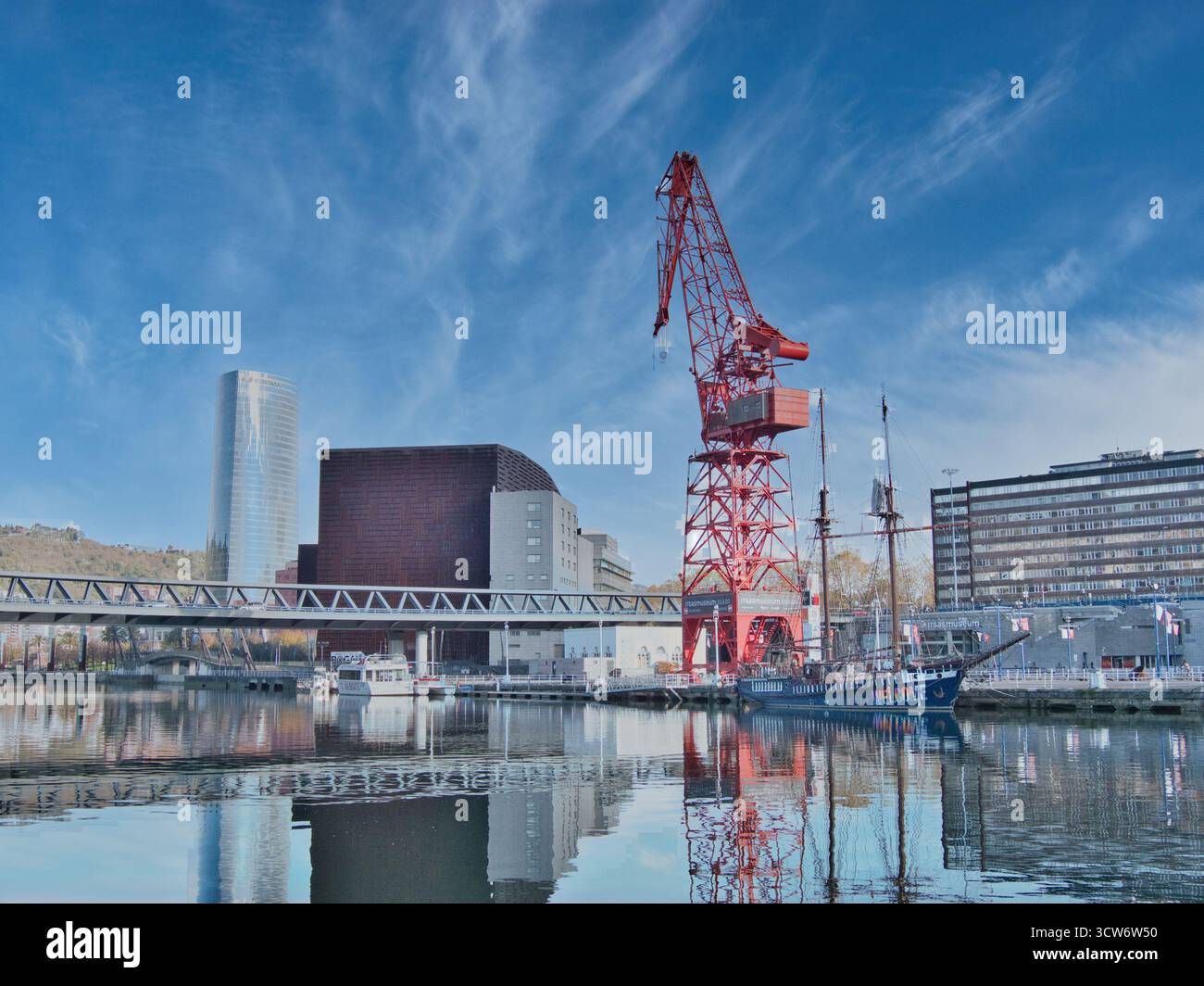 Bilbao Stadtbild mit Carola Crane - Blick auf die Bilbao Uferpromenade mit dem roten Carola-Kran und moderner Architektur, die sich im Nervion River, B, widerspiegelt Stockfoto