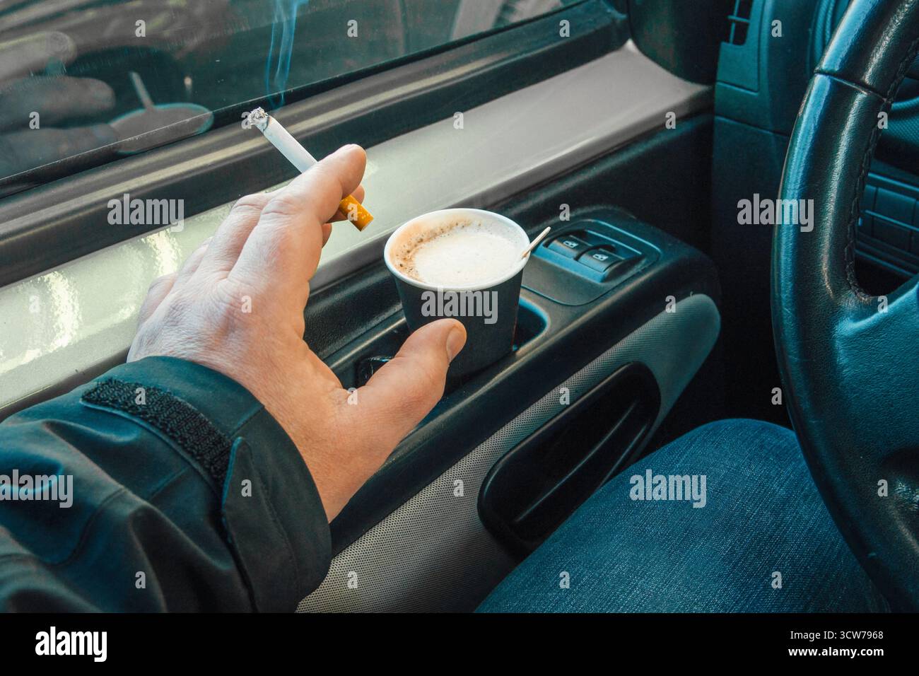 Rauchen im Auto. Die Hand eines Mannes mit einer rauchenden Zigarette in einer Kabine in Nahaufnahme Stockfoto