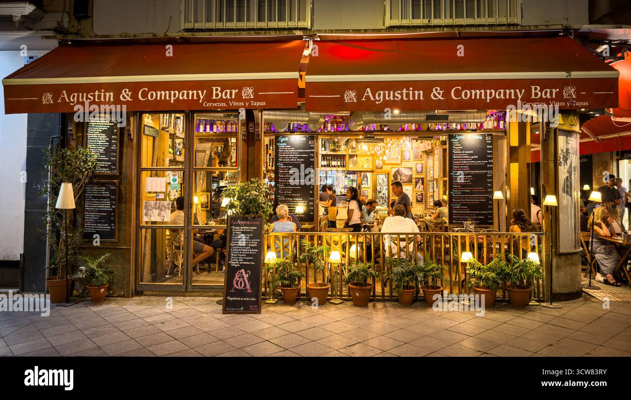 Sevilla, Spanien – 2. Oktober 2025: Blick auf die Straße von Agustín & Company Bar mit Sitzplätzen im Freien und Abendgästen Stockfoto