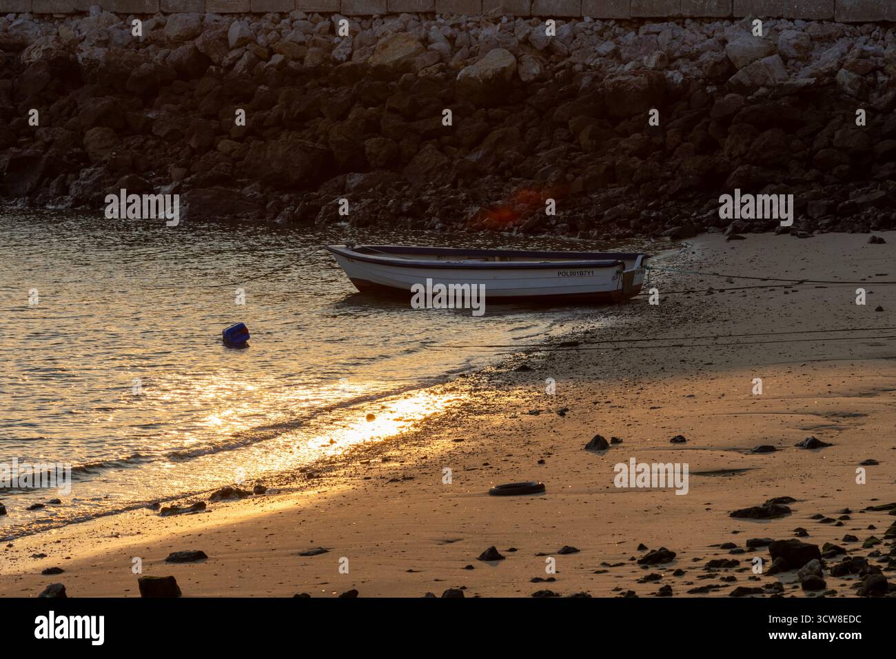 Weißes Fischerboot, das bei Sonnenuntergang an einem Sandstrand verankert ist, schafft eine friedliche und ruhige Küstenlandschaft Stockfoto