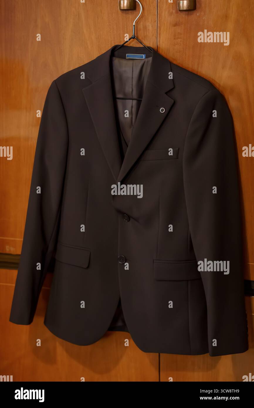 Ein gut gepresster brauner Herrenanzug hängt ordentlich in einer hölzernen Garderobe, was professionelle Mode, formelle Anlässe oder Business-Stil andeutet und sauber ist Stockfoto