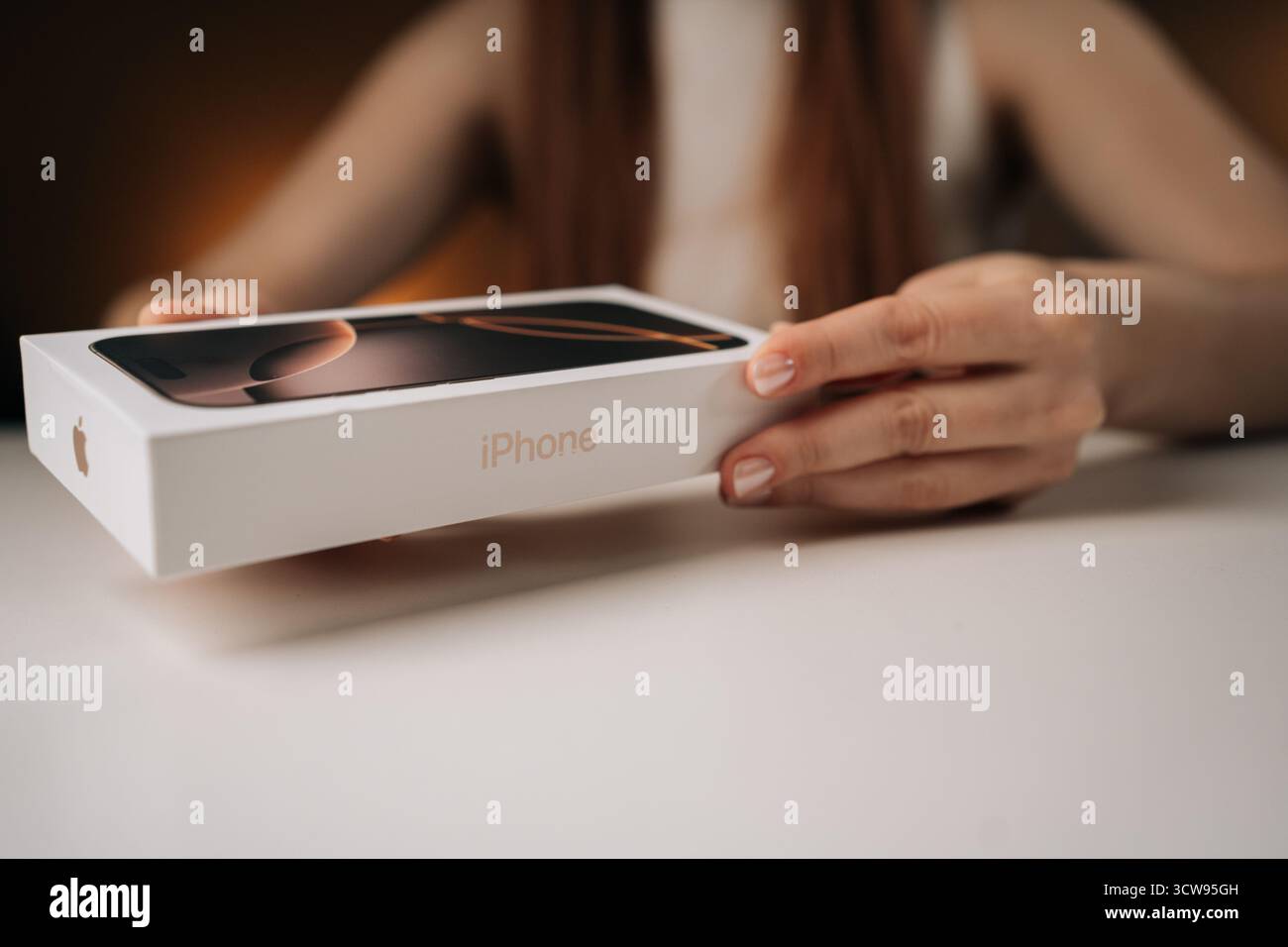 Nahaufnahme von jungen Frauenhänden, die das neueste iPhone 16 Pro auspacken und das moderne Smartphone-Design auf weißem Tisch enthüllen. Stockfoto