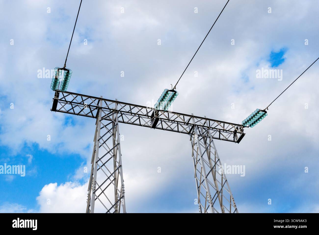 Stromübertragungsturm aus Stahl und grüne Isolatoren unter teilweise bewölktem, hellem Himmel Stockfoto