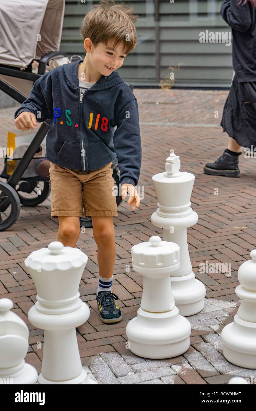 Lustiger, lächelnder kleiner Junge, der Schach auf dem Bürgersteig spielt Stockfoto