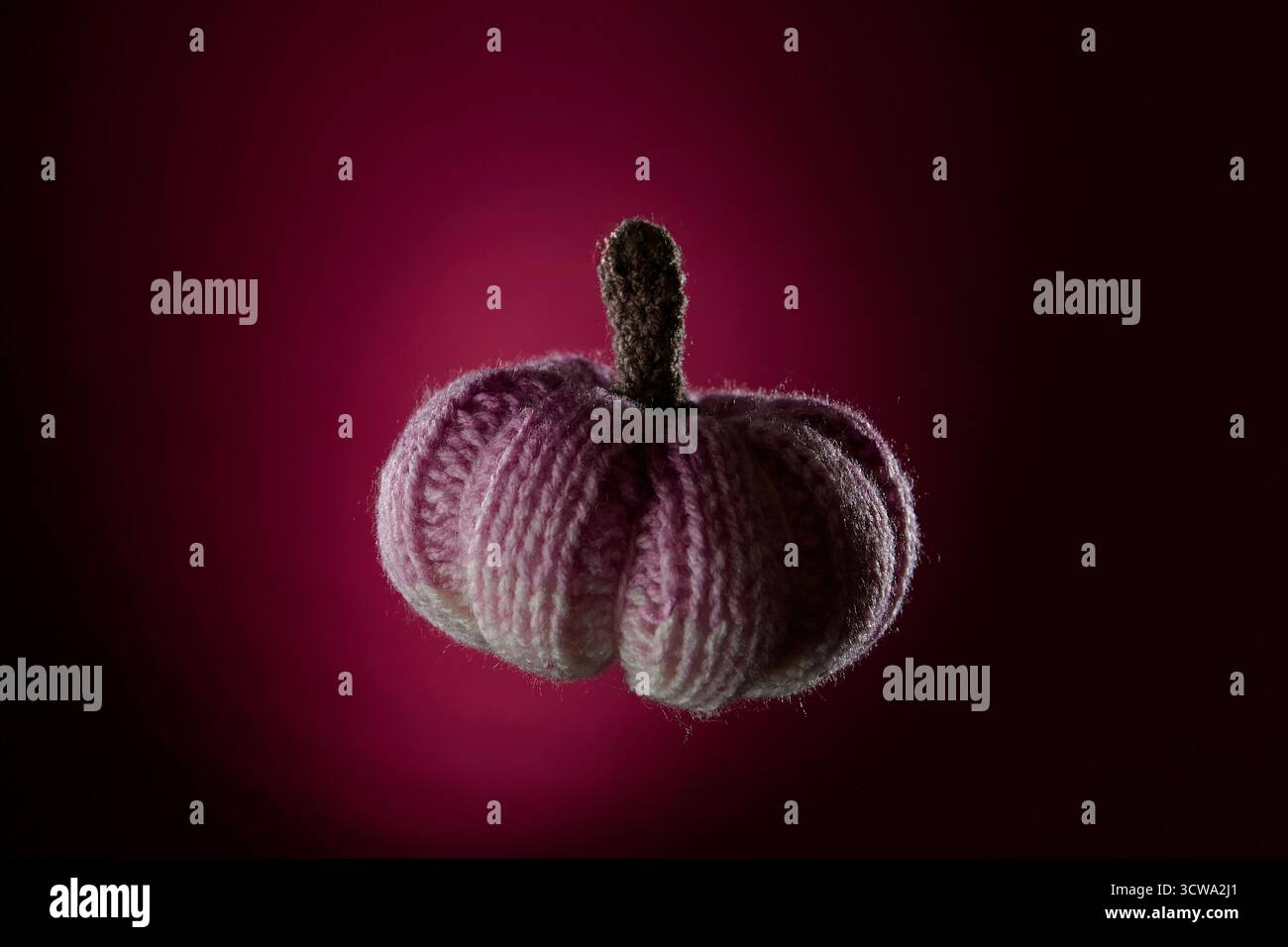 Handgefertigter rosa gestrickter Kürbis auf dunklem magentafarbenen Hintergrund. Gemütliches Kunsthandwerk mit Herbstdekor, Erntezeit und handgefertigter Kreativit Stockfoto
